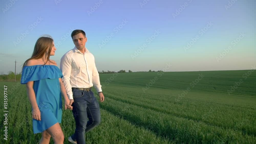 Couple in love walking on the spring wheat field and holds hands on sunset Couple in love walking on the spring wheat field and holds hands on sunset