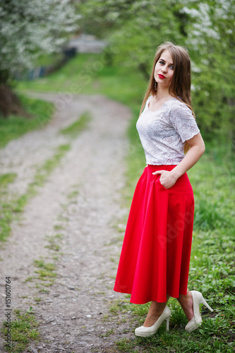 Portrait of beautiful girl with red lips at spring blossom garden, wear on red dress and white blouse.