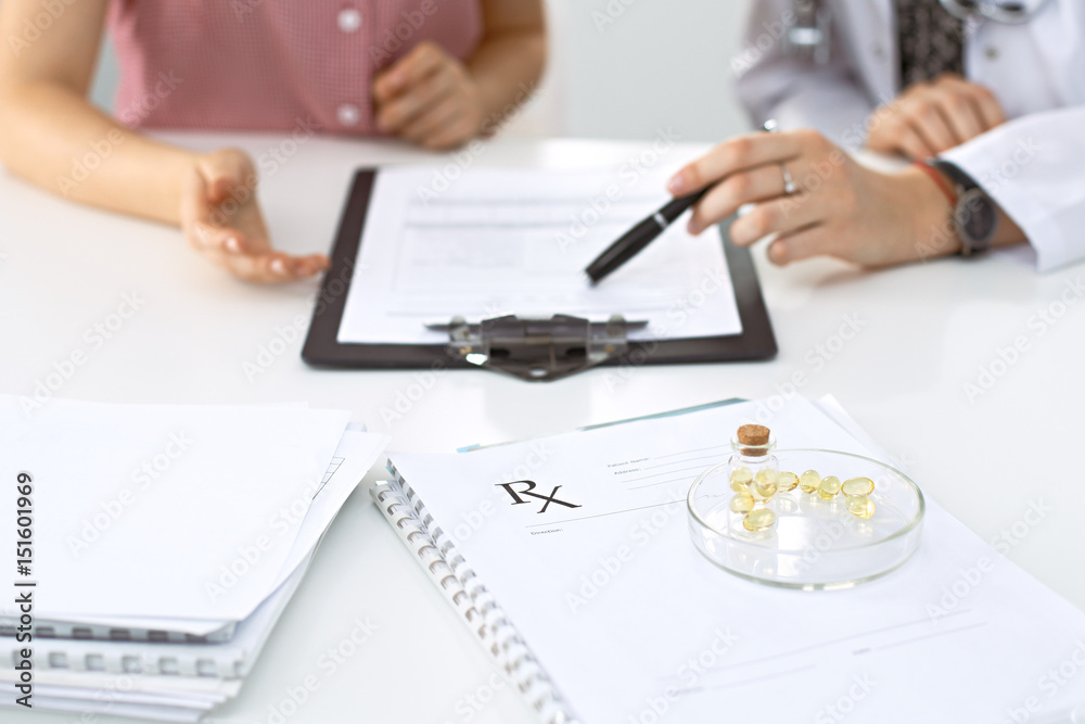 Medical prescription form, capsules and pills are lying against the background of a doctor and patient discussing health exam results Medical prescription form, capsules and pills are lying against the background of a doctor and patient discussing health exam results