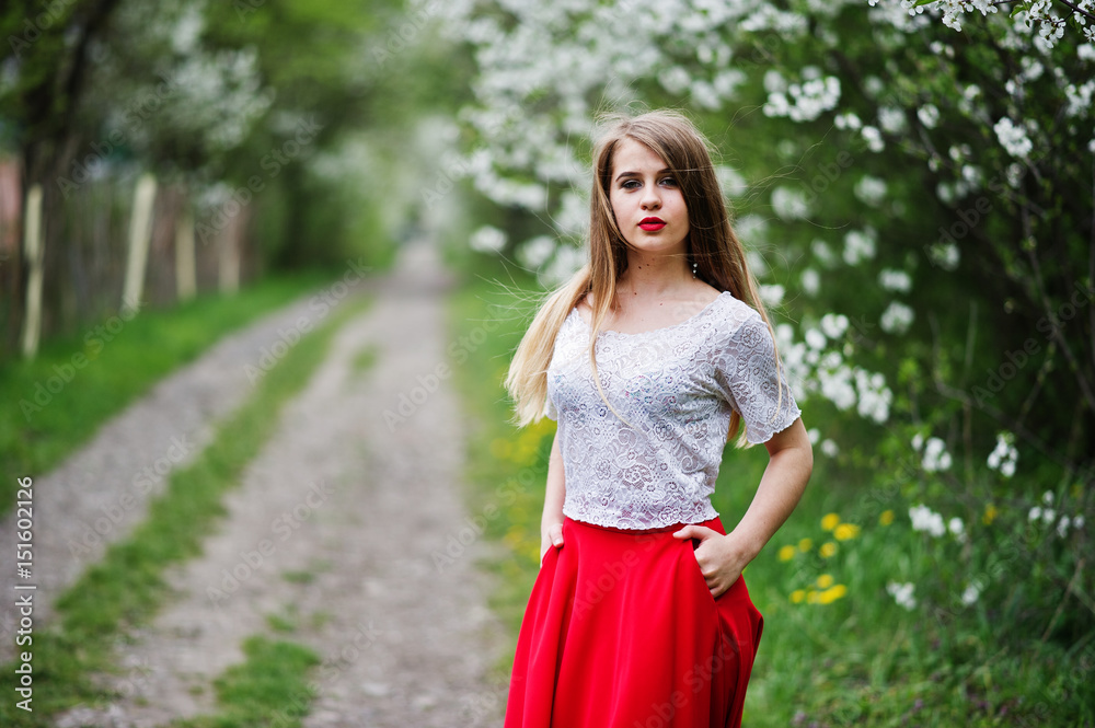 Portrait of beautiful girl with red lips at spring blossom garden, wear on red dress and white blouse.