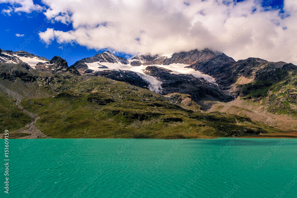 Lago Bianco and the mountains of the Bernina range at the Ospizio Bernina under white clouds in summer. This is the highest point on the Bernina Railwayline. Poschiavo, Engadin, Grisons, Switzerland Lago Bianco and the mountains of the Bernina range at the Ospizio Bernina under white clouds in summer. This is the highest point on the Bernina Railwayline. Poschiavo, Engadin, Grisons, Switzerland