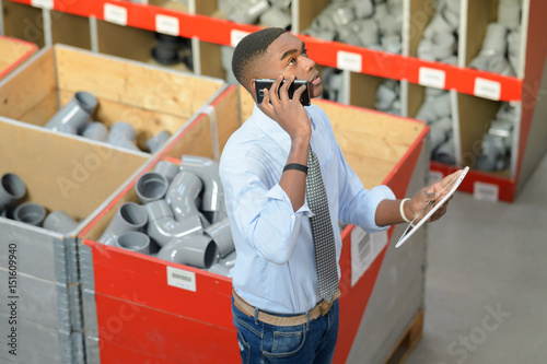 Man in pipe fittings department, holding tablet and speaking on telephone
