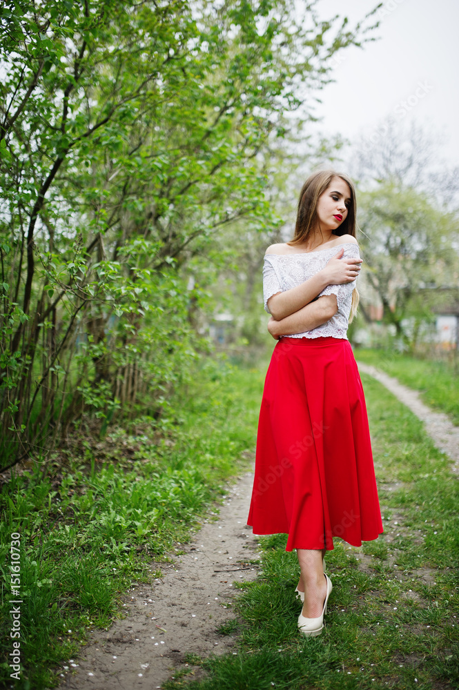 Portrait of beautiful girl with red lips at spring blossom garden, wear on red dress and white blouse.