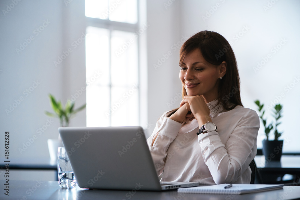 Attractive smiling young business woman using laptop at work desk Attractive smiling young business woman using laptop at work desk