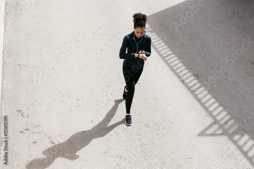 Young woman in sportswear walking on street and looking on her activity tracker photo
