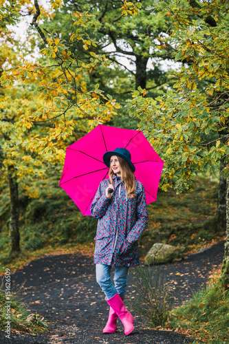 Young stylish woman stands on the road in park with pink umbrella