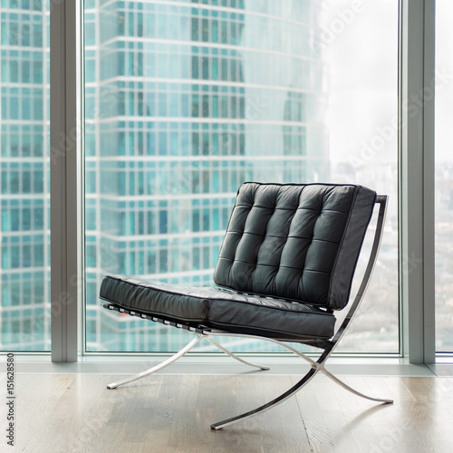Black leather armchair against big window with skyscraper on background
