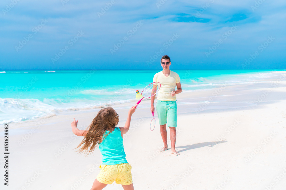 Little girl playing tennis with father on white tropical beach