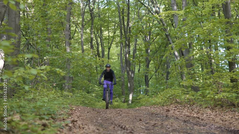 Young sports man riding bicycle on the tree forest road, stoped for rest, sunny spring day Young sports man riding bicycle on the tree forest road, stoped for rest, sunny spring day