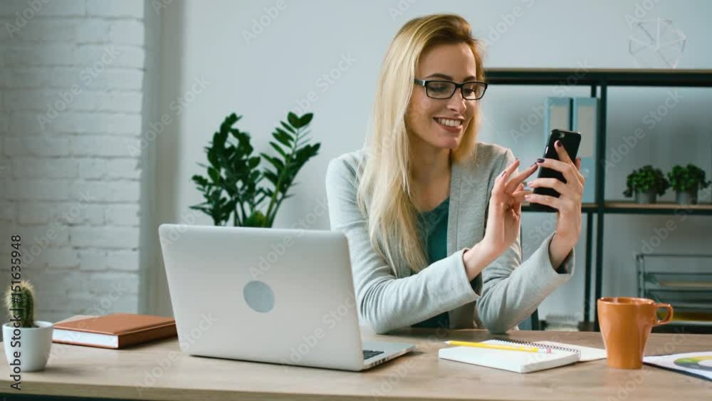 Beatiful emotional business woman sitting at the office table and chating with friends on smart phone in the office. Beatiful emotional business woman sitting at the office table and chating with friends on smart phone in the office.