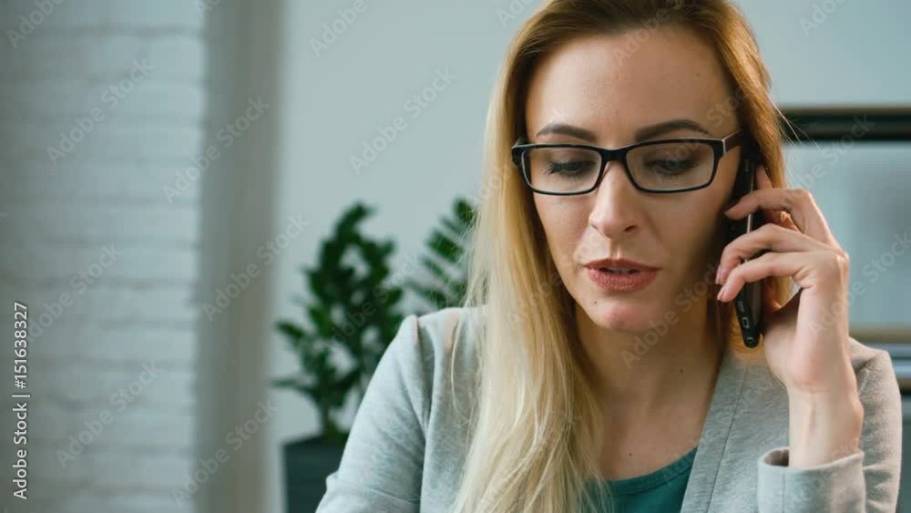 Beautiful stylish business woman in the glasses smiling and talking on the smart phone in the office. Close up. Beautiful stylish business woman in the glasses smiling and talking on the smart phone in the office. Close up.