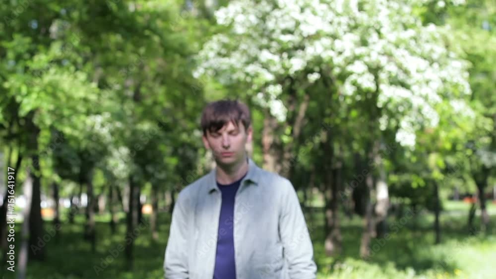 A lonely handsome guy walks through the park. He comes closer and looks at the camera A lonely handsome guy walks through the park. He comes closer and looks at the camera