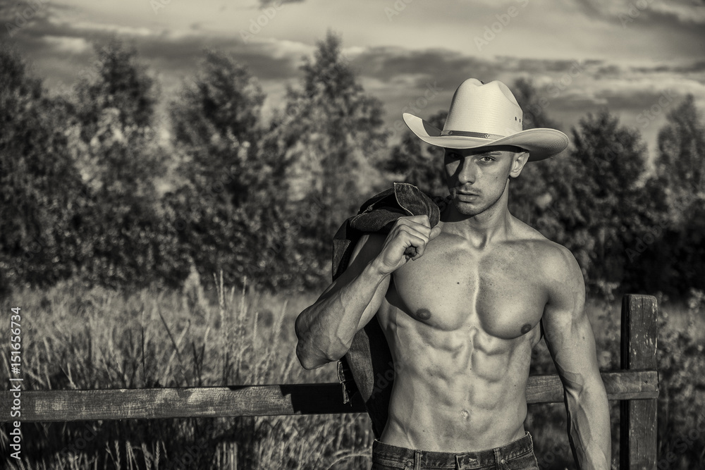 Portrait of sexy farmer or cowboy in hat looking to a side, while standing next to hay field in countryside Portrait of sexy farmer or cowboy in hat looking to a side, while standing next to hay field in countryside