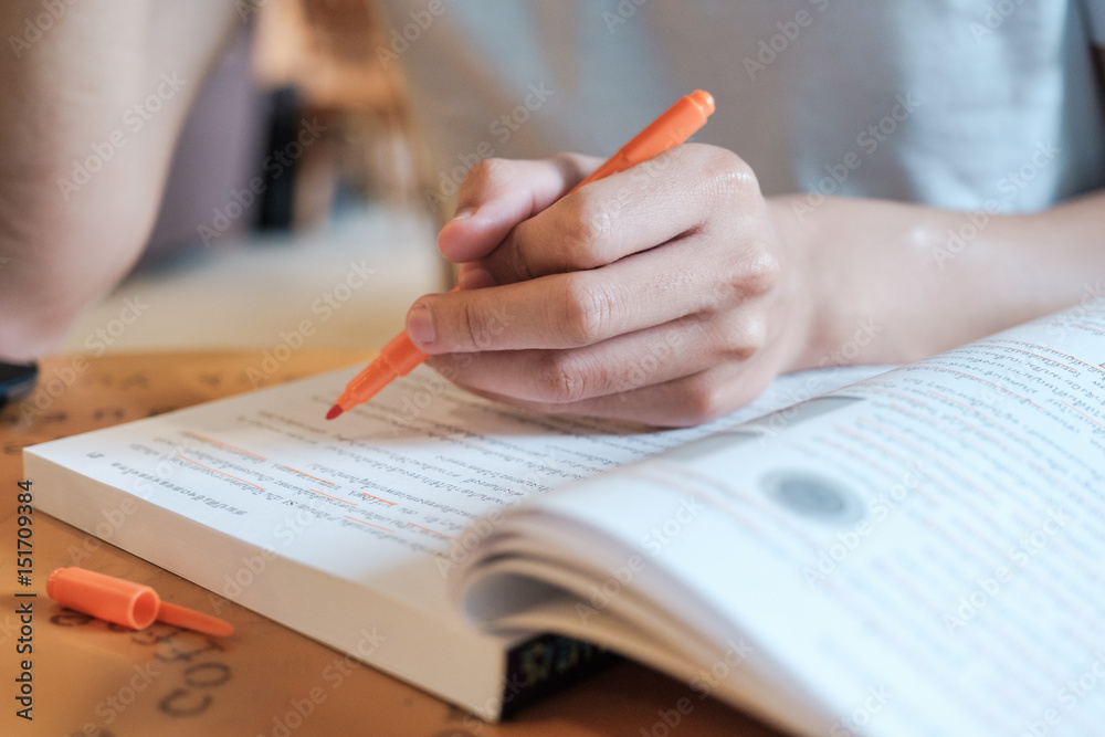 Young man holding a orange pen and reading a book in coffee shop Young man holding a orange pen and reading a book in coffee shop