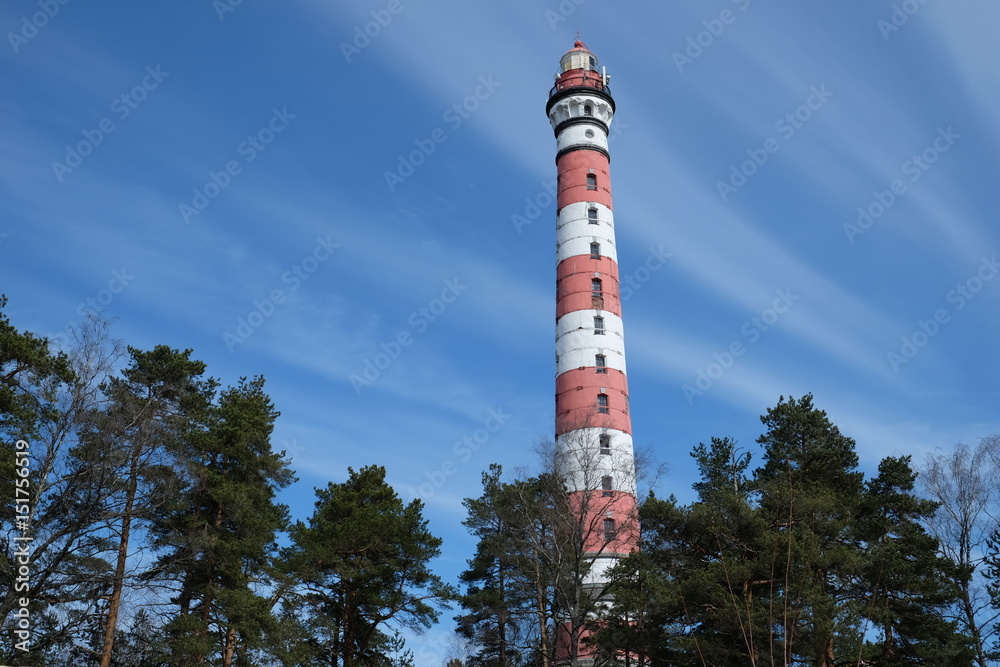 Old lighthouse snanding in the forest near the Baltik sea. Blue sky and green trees.