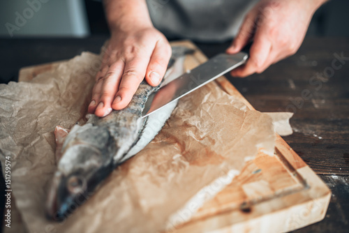 Chef hands with knife cut up fish on cutting board