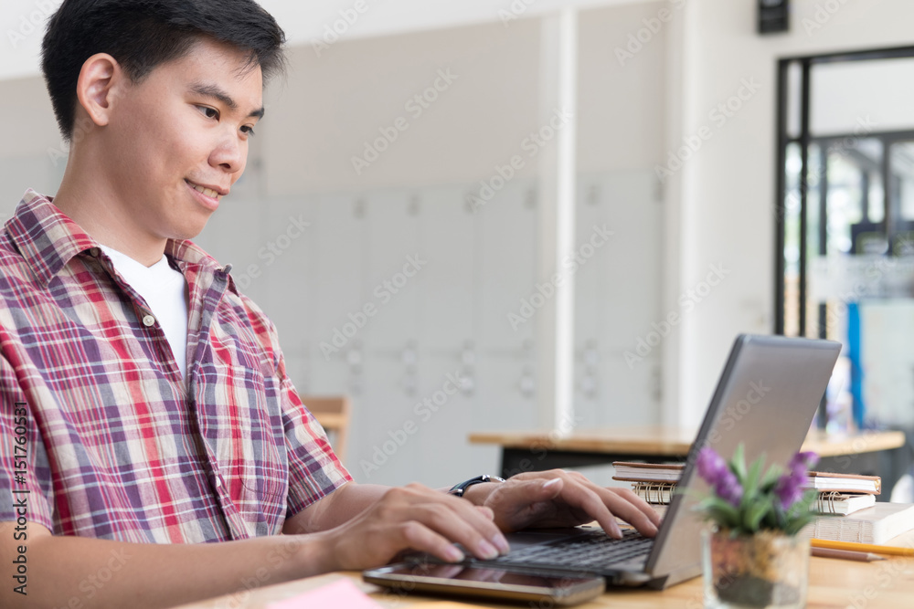 student sitting in room and typing on keyboard while looking at computer, handsome young asian man using laptop in cafe student sitting in room and typing on keyboard while looking at computer, handsome young asian man using laptop in cafe