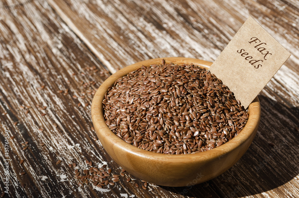 Close up of brown flax seeds in wooden bowl with tag on a rustic table. Superfood: linseeds are high in omega-3 fatty acids, essential for good health. Healthy eating ,vegan diet concept. Close up of brown flax seeds in wooden bowl with tag on a rustic table. Superfood: linseeds are high in omega-3 fatty acids, essential for good health. Healthy eating ,vegan diet concept.