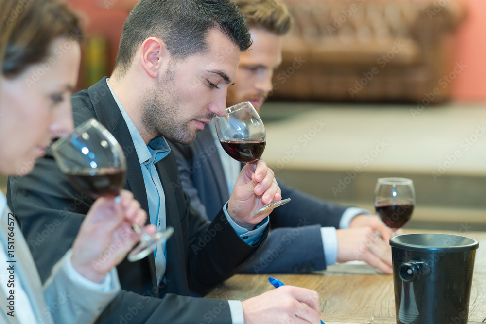 three people smelling and evaluating red wine in wineglasses three people smelling and evaluating red wine in wineglasses