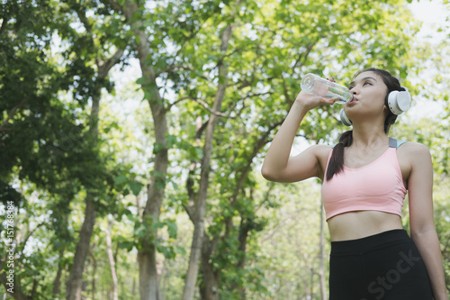young beautiful asian fitness athlete woman drinking water after work out exercising at summer green park.