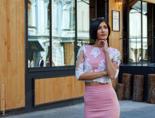A fashionable girl in a pink blouse and skirt, looks with interest at the sights on the city street