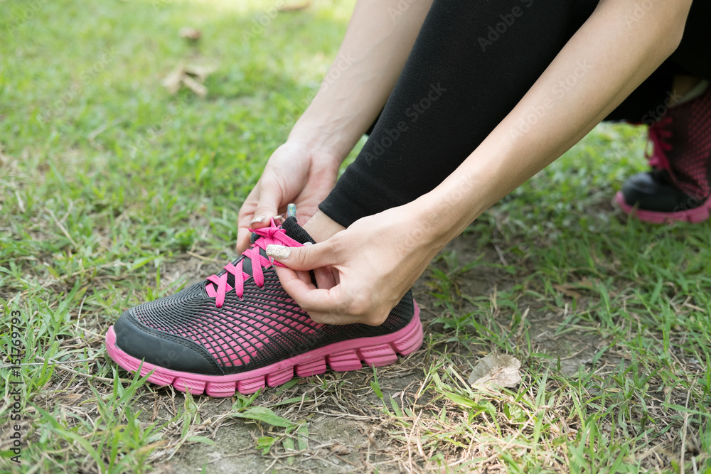 Urban athlete woman tying running shoe laces. Female sport fitness runner getting ready for jogging outdoors on forest path in city park