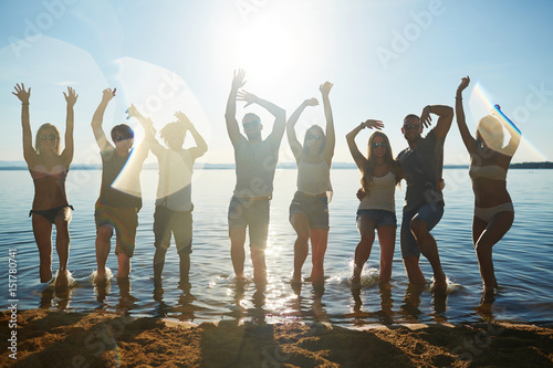 Energetic friends dancing in water by sandy beach