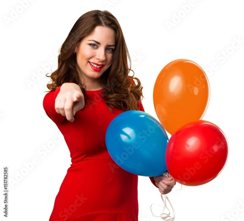 Beautiful young girl holding balloons and pointing to the front © luismolinero