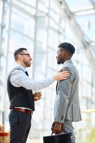Schilderij op canvas Portrait of smiling businessman chatting with African-American partner patting h