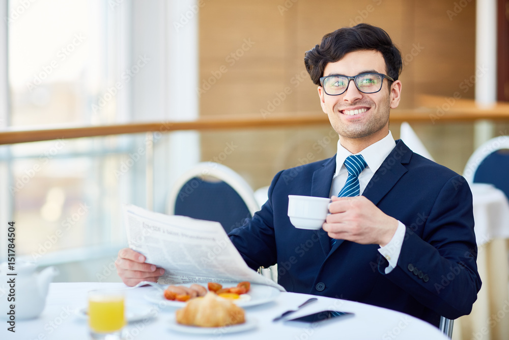 Cheerful businessman with drink and newspaper sitting in cafe Cheerful businessman with drink and newspaper sitting in cafe