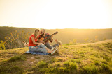 Lovers in nature. Young couple in love sitting on the park  while these young guitar playing guitar in sunset time. Together with dogs