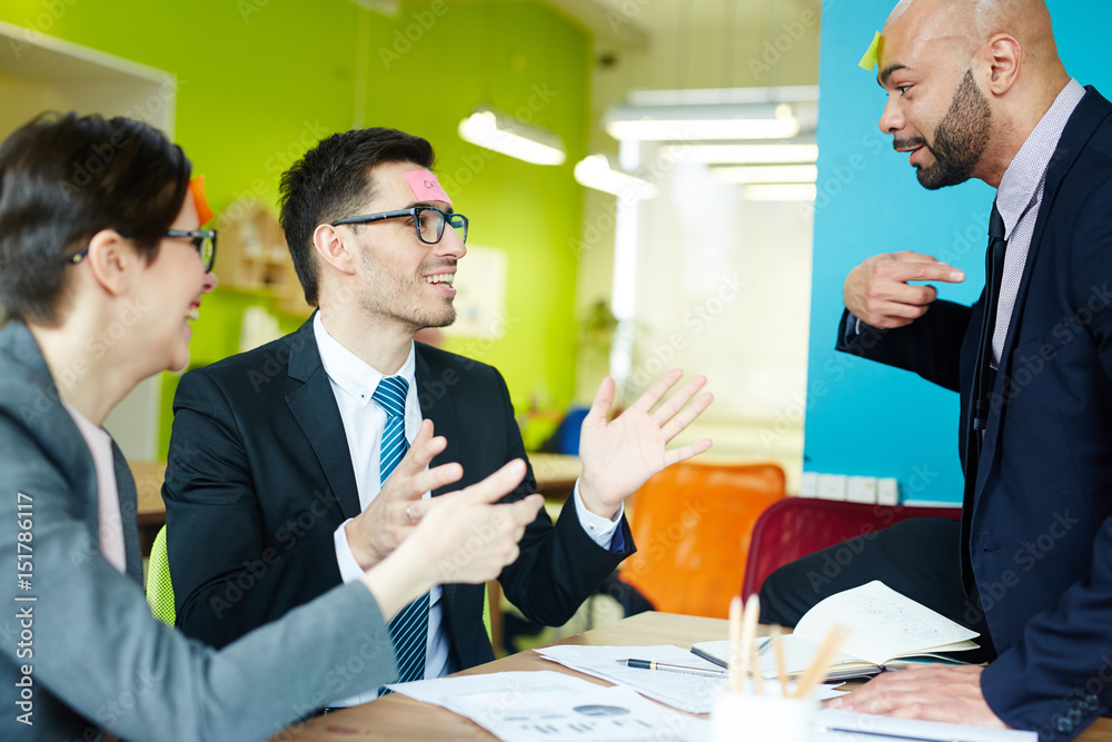 Modern colleagues playing humorous game with sticky notepapers Modern colleagues playing humorous game with sticky notepapers