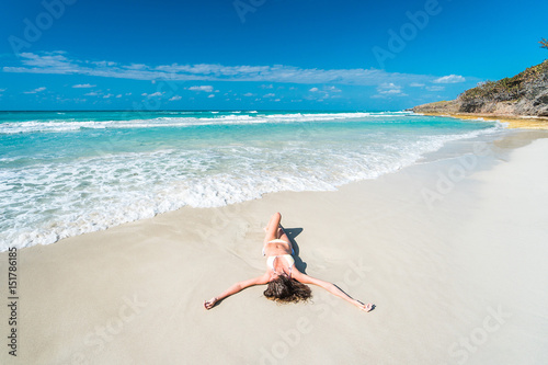 Beautiful young woman with long blond hair in white bikini swimsuit is lying on the sand of caribbean beach