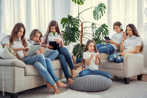 Kids with phones and tablets, with smartphones and headphones. Group of teenage girls is using gadgets.