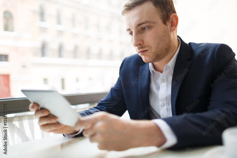 Portrait of modern businessman wearing formal suit using digital tablet at table in cafe and looking at screen Portrait of modern businessman wearing formal suit using digital tablet at table in cafe and looking at screen