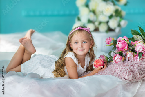 Nice looking young girl lady in cute dress sitting on a sofa with flowers in white stylish dress.
