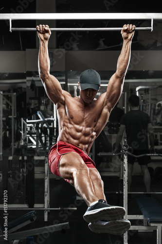 Fotografia Muscular man working out in gym, doing stomach exercises on a horizontal bar, st
