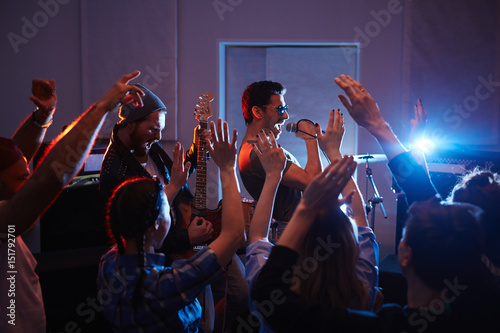 Handsome musicians rocking on stage of urban club with crowd cheering and dancing people partying raising arms