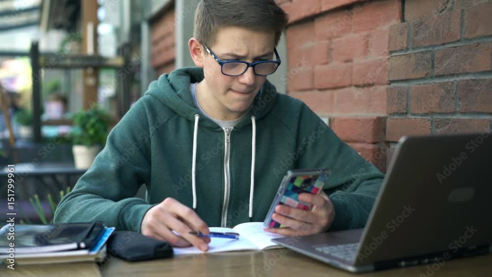 Boy with smartphone and notepad doing homework by table in cafe
Boy with smartphone and notepad doing homework by table in cafe