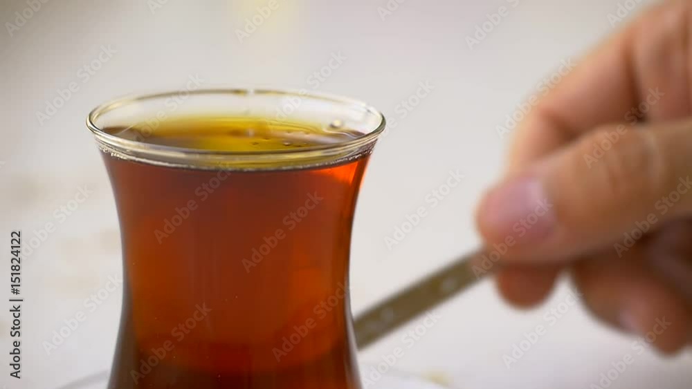 Slow Motion, Close up of Stirring a glass of hot tea to dissolve the sugar I've just added. Turks use special curved, see-through tea glasses. A small plate underneath for making tea easier to carry a Slow Motion, Close up of Stirring a glass of hot tea to dissolve the sugar I've just added. Turks use special curved, see-through tea glasses. A small plate underneath for making tea easier to carry a