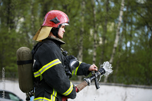 Fireman in fire fighting suit spraying water to fire surround