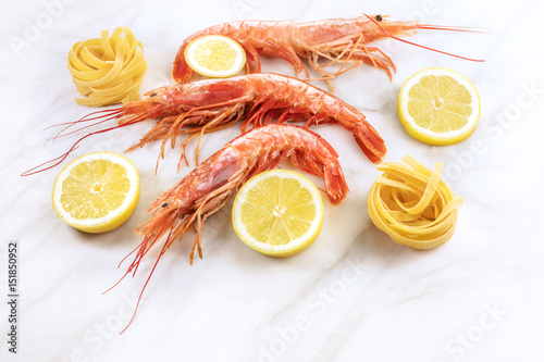 Raw shrimps with lemon and pasta on marble table