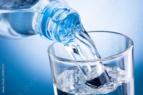 Close-up pouring water from bottle into glass on blue background