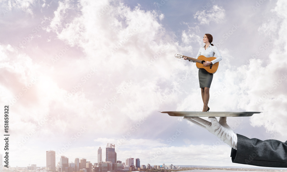 Attractive businesswoman on metal tray playing acoustic guitar against cityscape background Attractive businesswoman on metal tray playing acoustic guitar against cityscape background