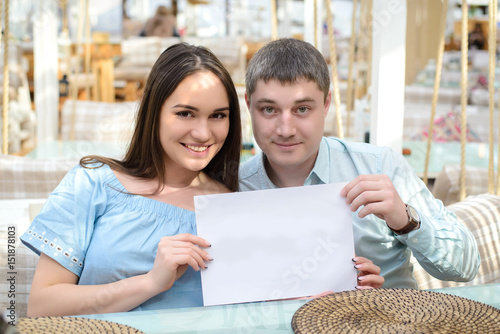 A guy and a girl looking at the camera and holding a blank piece of paper