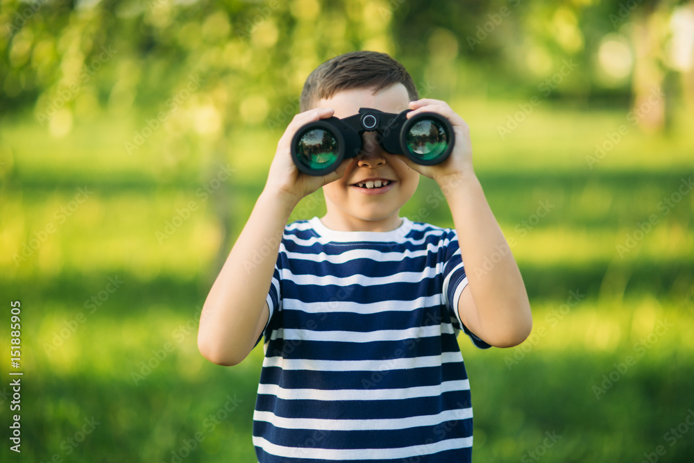Little boy in a striped t-shirt looks through binoculars .Spring, sunny weather.