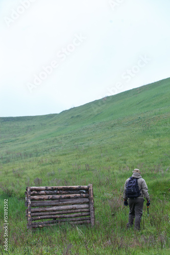 Male traveler with an ax and a backpack on a background of green mountains and firewood. © Vadym Sarakhan