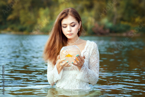 Woman makes a wish, in her hands a goldfish in an aquarium. photo