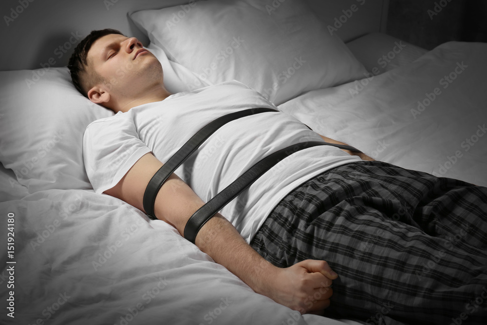 Young man tied up with belts in bed Stock Photo | Adobe Stock