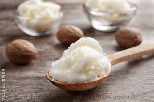 Shea butter in spoon and bowls on wooden background, close up photo